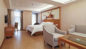 Quarto de hotel com uma cama, duas poltronas, uma mesa de centro de vidro, uma escrivaninha e uma televisão.