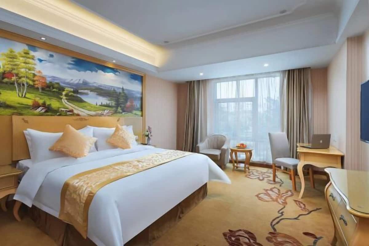 A hotel room with a large bed, a desk, a chair, and a television.
