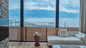 A modern room with a large window, a sofa, a small table, and a view of mountains and water. - Dali Hidden in the Clouds Lake View Hotel (Dali City)