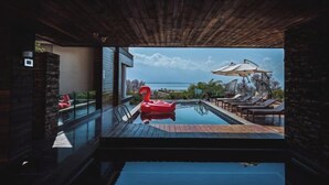 An infinity pool with a red flamingo float, lounge chairs, and umbrellas, overlooking a body of water. - Dali Hidden in the Clouds Lake View Hotel (Dali City)