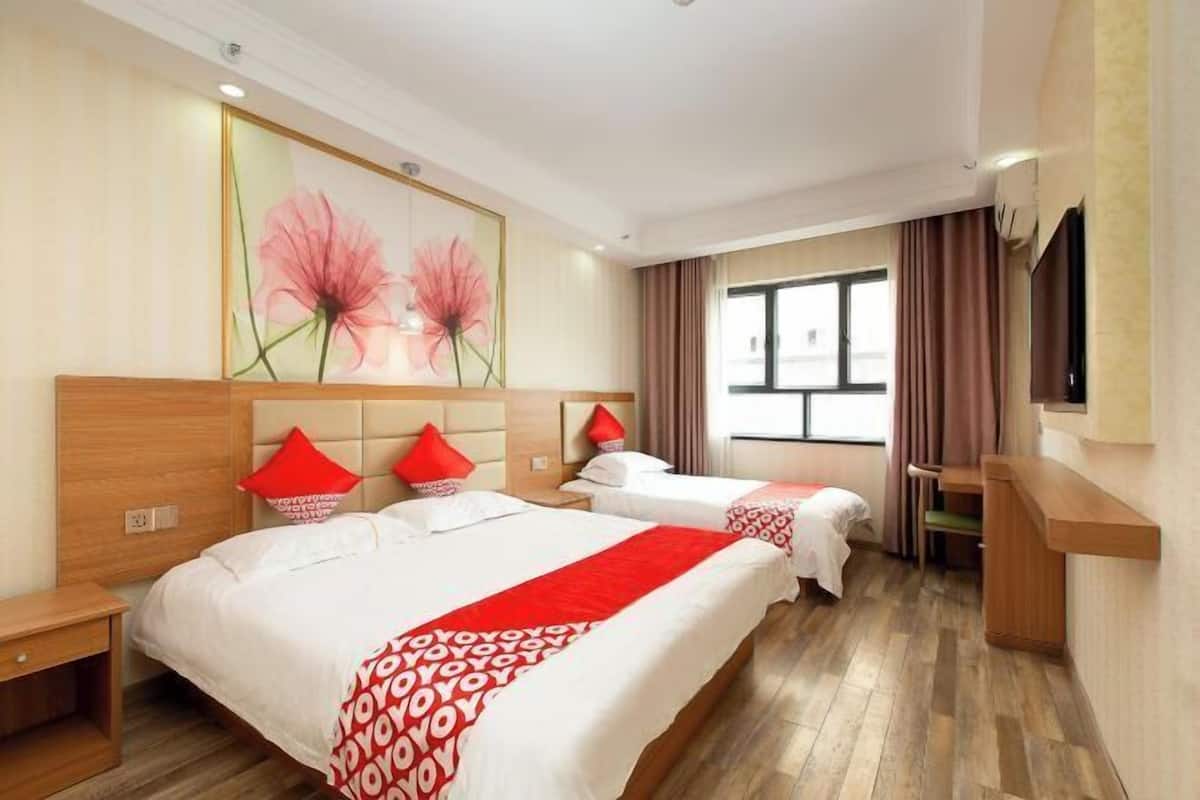 A hotel room with two beds, a wooden headboard, a large window with curtains, and a painting on the wall.