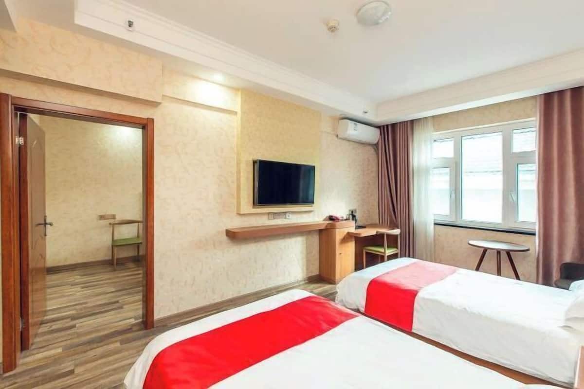 A hotel room with two beds, a TV, a desk, a chair, and a window.