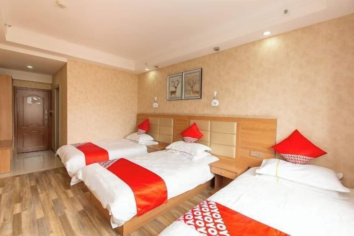 A hotel room with three beds, wooden headboards, and red pillows.