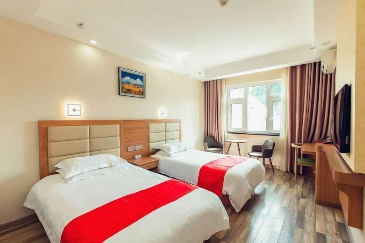 A hotel room with two beds, a desk, a chair, a television, and a window with curtains.