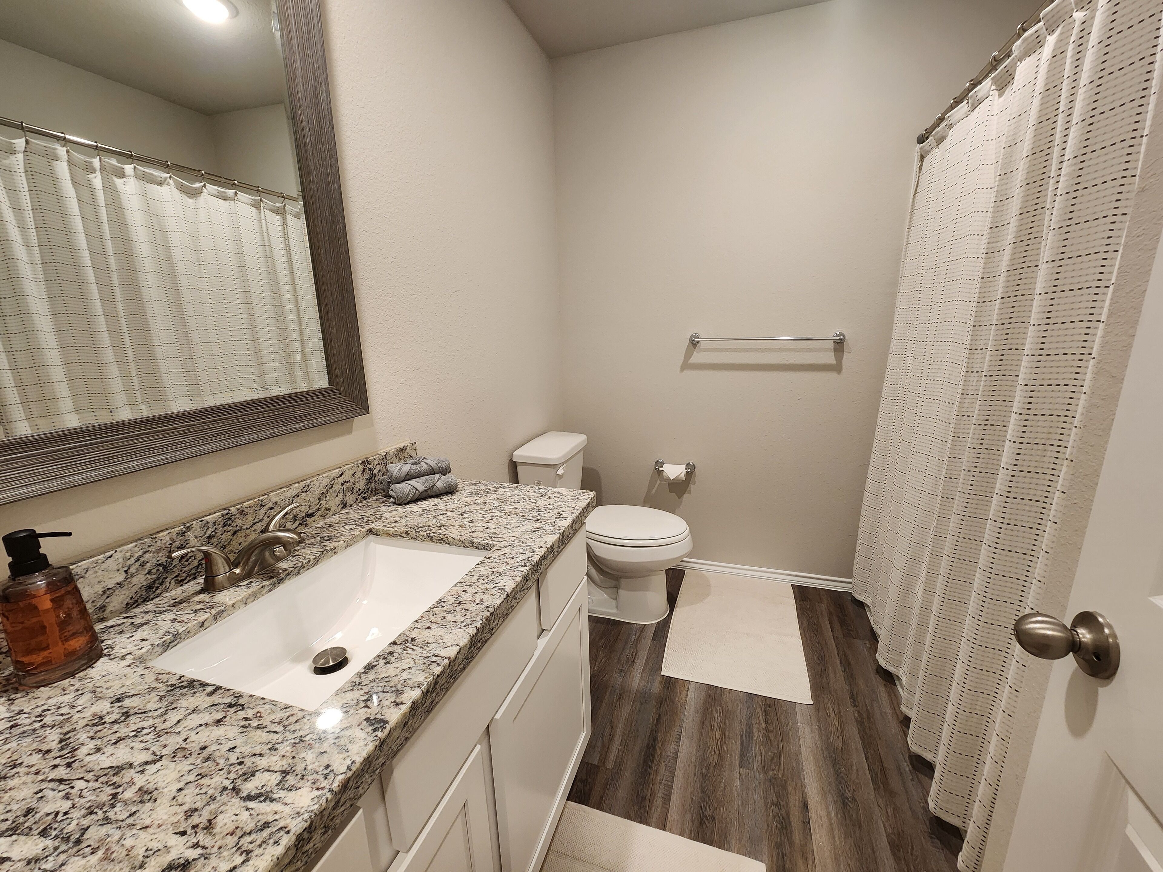A bathroom with a granite countertop sink, a toilet, and a shower curtain.