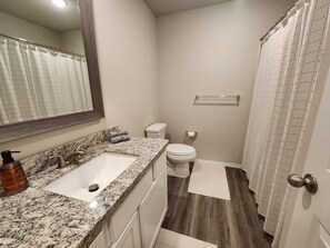 Un baño con lavamanos de encimera de granito, inodoro y cortina de ducha.