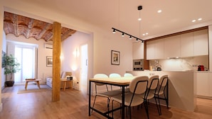 A modern kitchen with white cabinets, a wooden dining table, and four chairs. - Reina Sofia Suite II (Madrid)