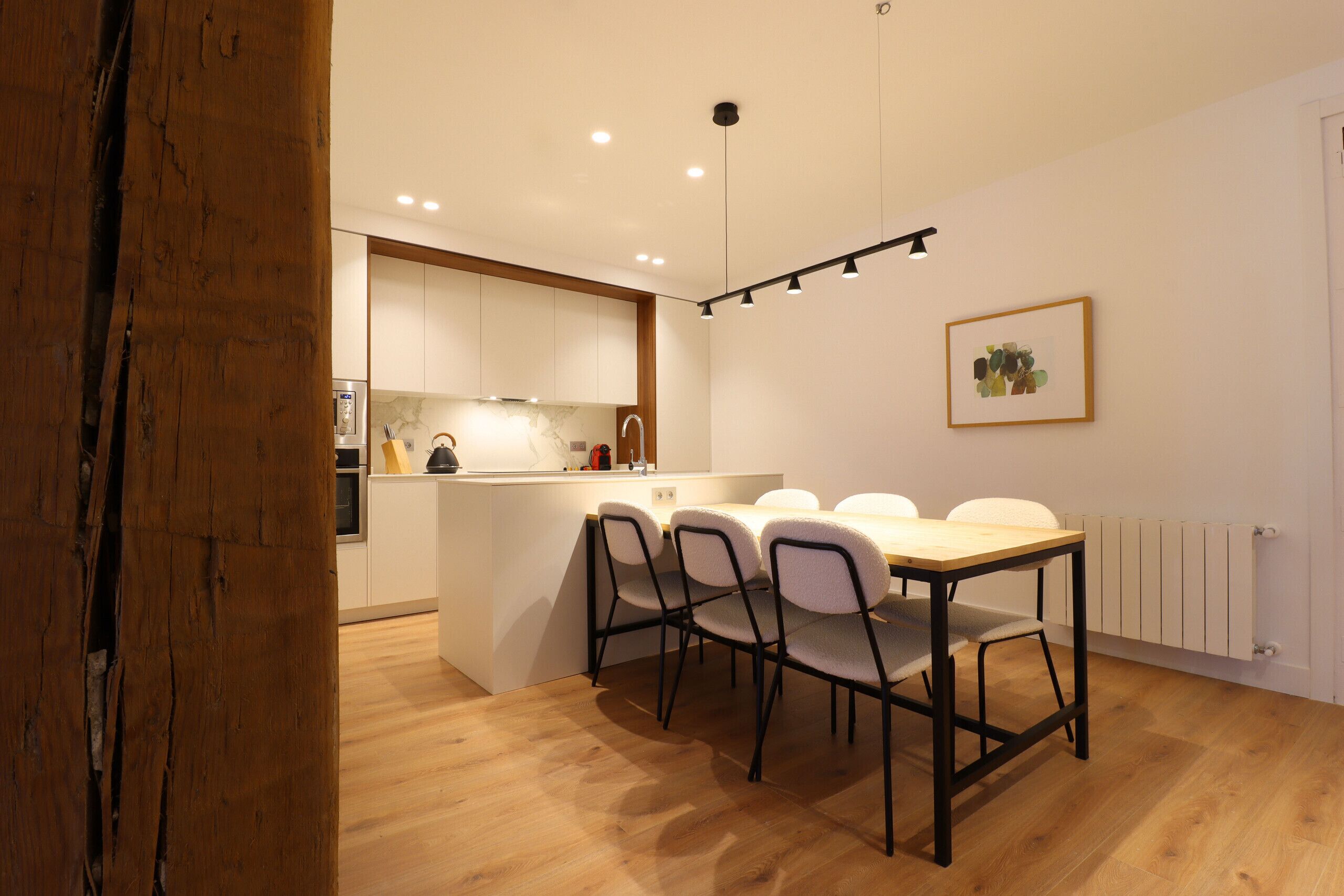 Een moderne keuken met witte kasten, een houten eettafel en vier stoelen.