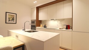 A modern kitchen with white cabinetry, a marble countertop, and a built-in oven. - Reina Sofia Suite II (Madrid)