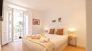 A spacious bedroom with a large bed, a bedside table with a lamp, and a view of the outdoors through a sliding door. - Reina Sofia Suite II (Madrid)