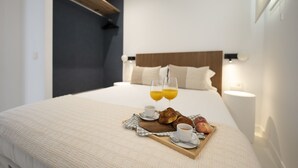 A neatly made bed with a breakfast tray including croissants, fruit, and two glasses of orange juice. - Reina Sofia Center (Madrid)