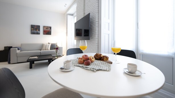 A modern living room with a round dining table set for breakfast, featuring croissants, a cup of coffee, and a glass of orange juice. - Reina Sofia Center (Madrid)