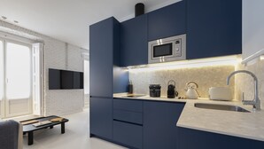 A modern kitchen with dark blue cabinets, a stainless steel microwave, a coffee maker, and a toaster. - Reina Sofia Center (Madrid)