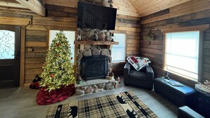 Interior acogedor de una cabaña de troncos con chimenea de piedra, un árbol de Navidad y un área de estar confortable.