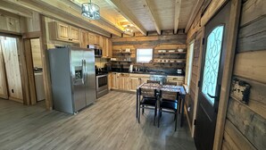 Una cocina rústica de estilo cabaña con paredes de madera, un refrigerador empotrado, una mesa de comedor con sillas y un ventanal con detalles decorativos.