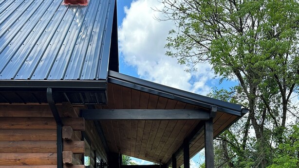 Una cabaña de troncos con terraza de madera, mobiliario exterior y techo de metal.