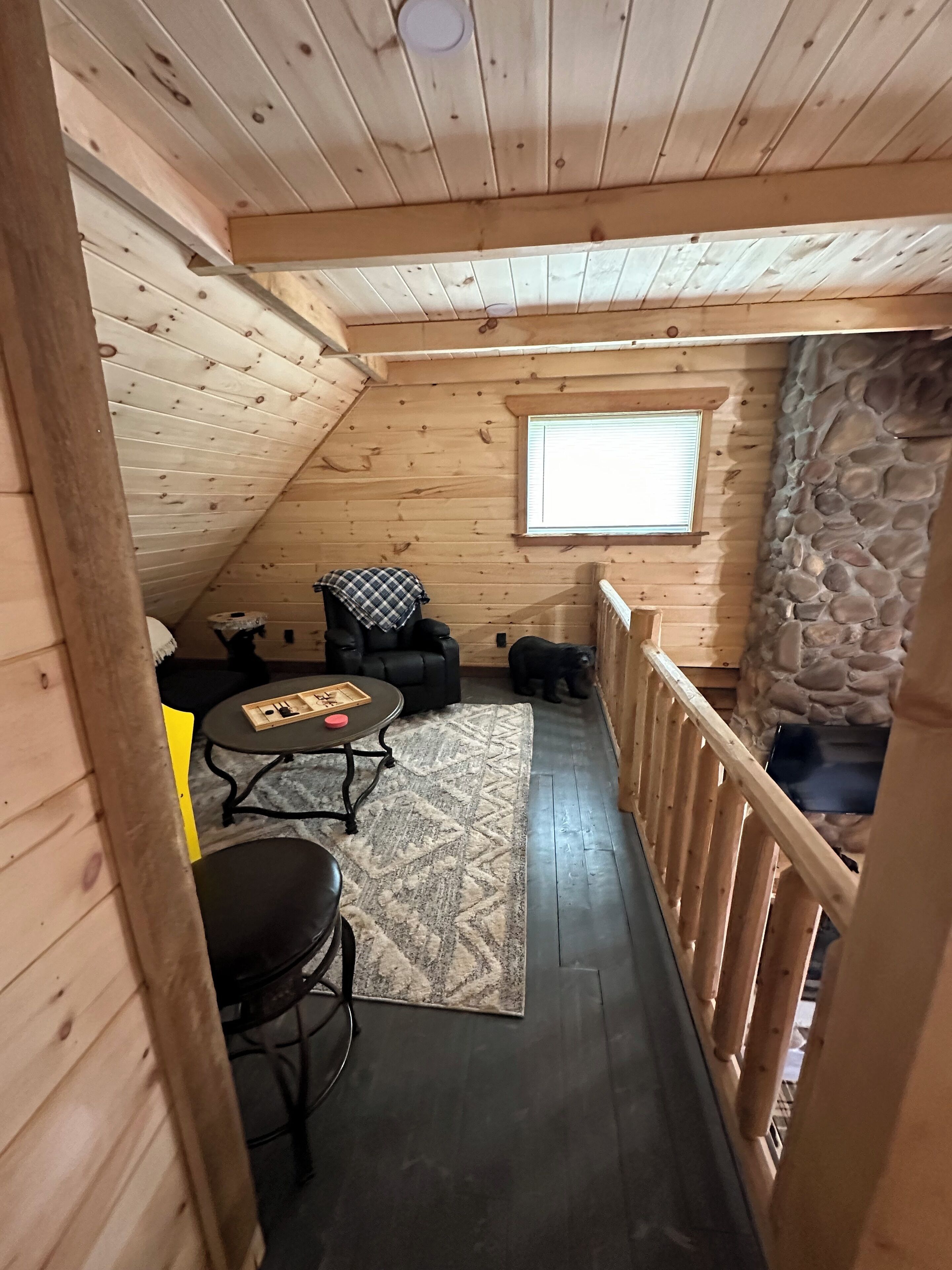 Een gezellig vakantiehuisje met houten inrichting, een stenen muur, een klein raam en een eethoek met een tafel en stoelen.