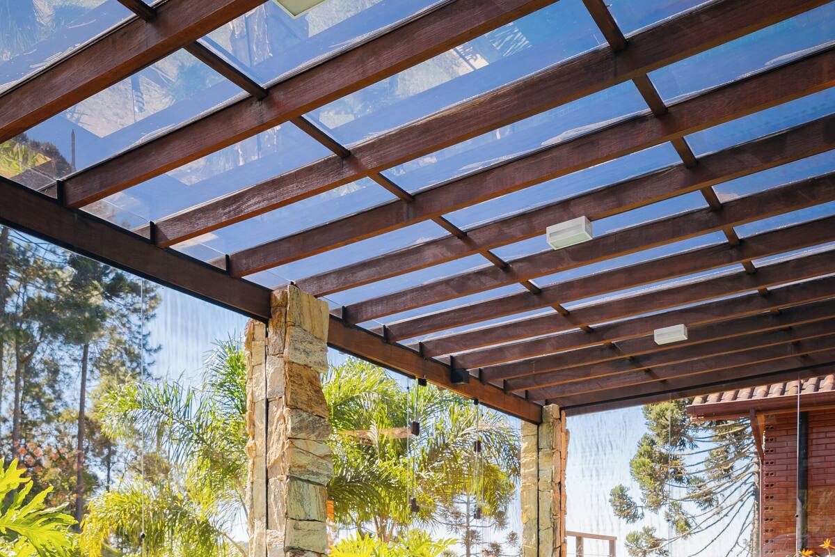 An indoor swimming pool with clear blue water, surrounded by stone pillars and glass panels, under a wooden pergola.