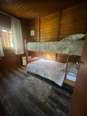 Une chambre avec des lits superposés, des murs en bois, une fenêtre avec des rideaux et un tapis sur le sol.
