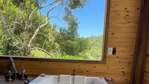 A wooden cabin with a hot tub and a large window overlooking a forest. - Pousada Rancho Queimado (Aguas Mornas)
