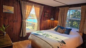 Ein Schlafzimmer mit einem großen Bett, Holzwänden, einem Fenster mit Vorhängen, einer Nachttischlampe und einem Bild an der Wand.