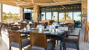 Ein Restaurant mit Außenbereich, Tischen, die mit Tellern, Gläsern und Besteck gedeckt sind, und Blick auf Palmen und eine Wüstenlandschaft.