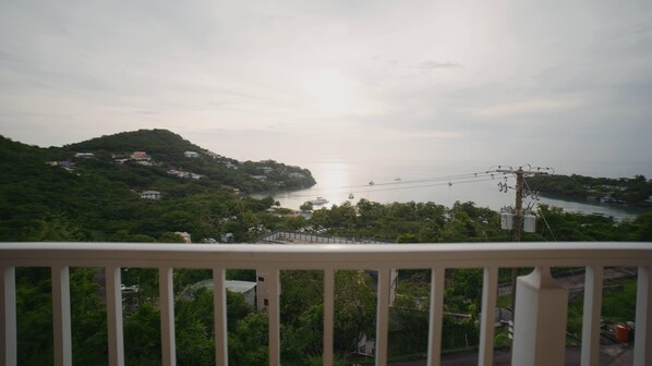 A coastal landscape with a view of the sea, a bridge, and a hill with buildings.
