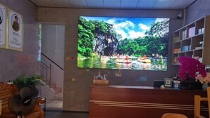 A reception area with a large TV displaying a nature scene, wooden furniture, and a reception desk.
