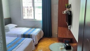 A hotel room with two beds, a small table, a TV, and a window with curtains.