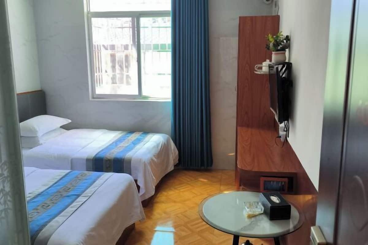 A hotel room with two beds, a small table, a TV, and a window with curtains.