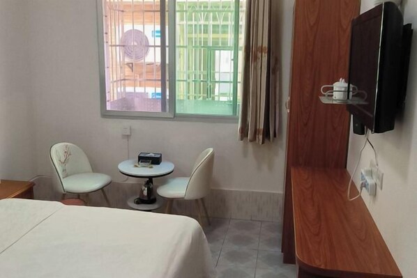 A hotel room with a bed, a small round table with two chairs, a television mounted on the wall, and a window with a view of the outside.