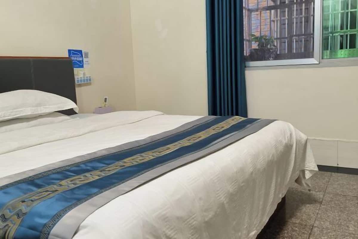 A hotel room with a bed, a nightstand, a window with curtains, and a wall-mounted sign.