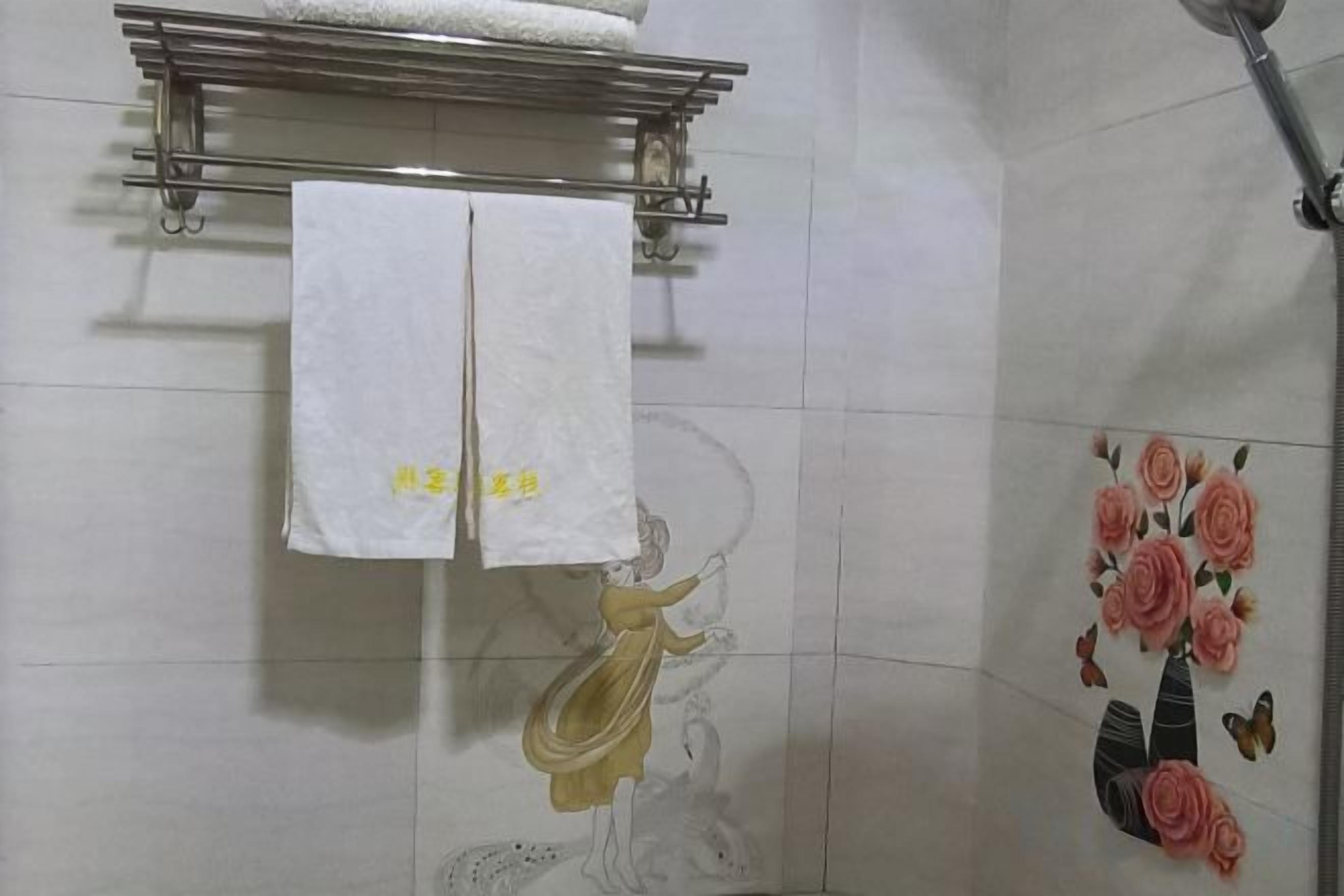 A bathroom with a towel rack holding two white towels, a shower area with a floral tile design, and a wall-mounted towel rack above the shower.