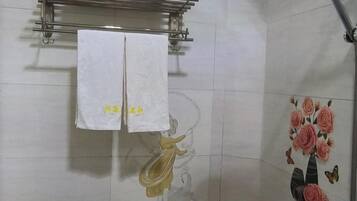 A bathroom with a towel rack holding two white towels, a shower area with a floral tile design, and a wall-mounted towel rack above the shower.