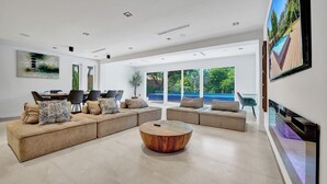A spacious living room with a large sectional sofa, a round coffee table, and a large TV screen. - Spacious 6-bedroom villa - with Outdoor Oasis - Pool in charming Fort Lauderdale (Fort Lauderdale)