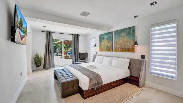 A modern bedroom with a large bed, a bench, a TV, and a painting. - Spacious 6-bedroom villa - with Outdoor Oasis - Pool in charming Fort Lauderdale (Fort Lauderdale)