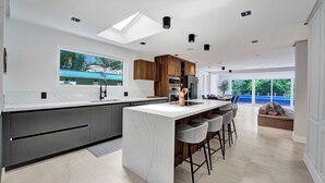 A modern kitchen with a large island, dark cabinetry, and a view of a swimming pool. - Spacious 6-bedroom villa - with Outdoor Oasis - Pool in charming Fort Lauderdale (Fort Lauderdale)