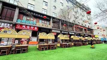 A row of outdoor tables and chairs in front of a building with multiple shops and signs.