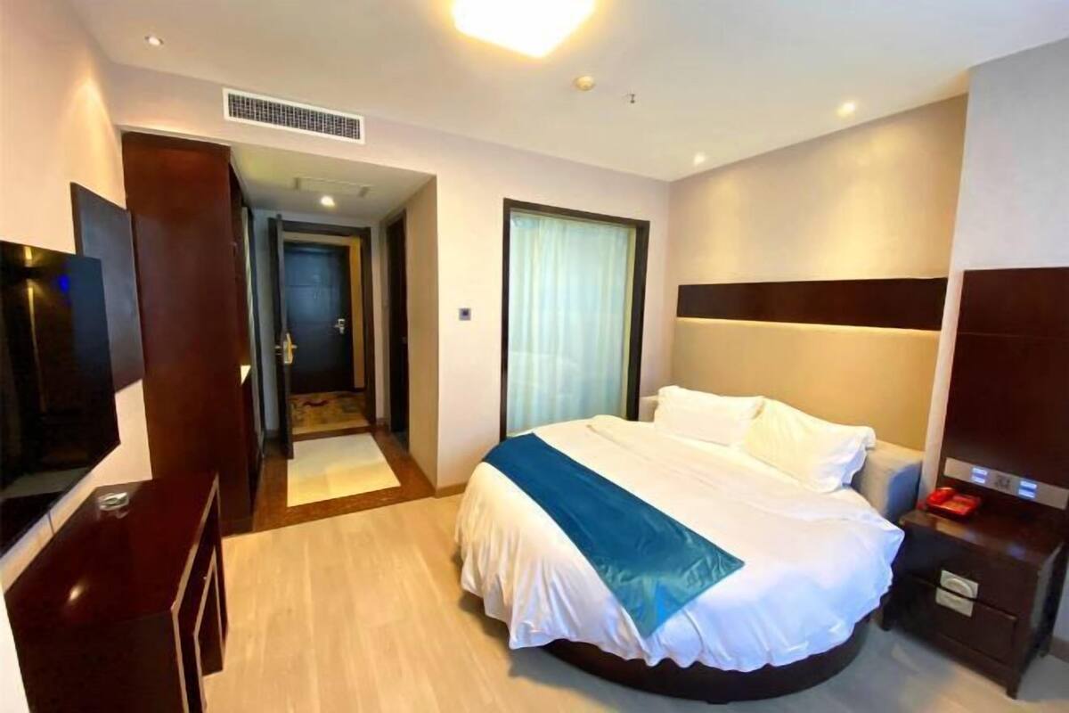 A hotel room with a large bed, a bedside table, a TV, and a door leading to a hallway.