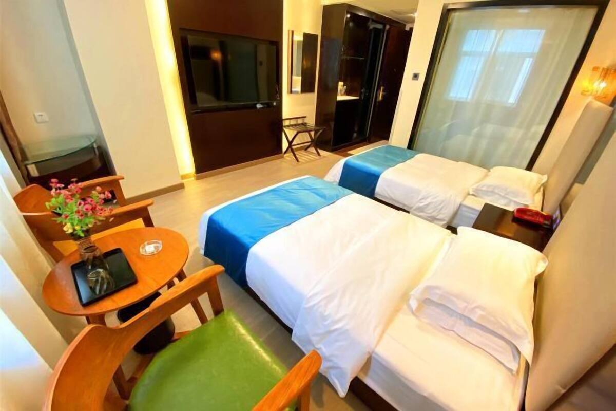 A hotel room with two beds, a desk, a chair, and a TV.