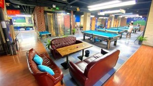 Una sala de billar con mesas de pool, asientos de cuero y una mesa de madera con una bola rosa.