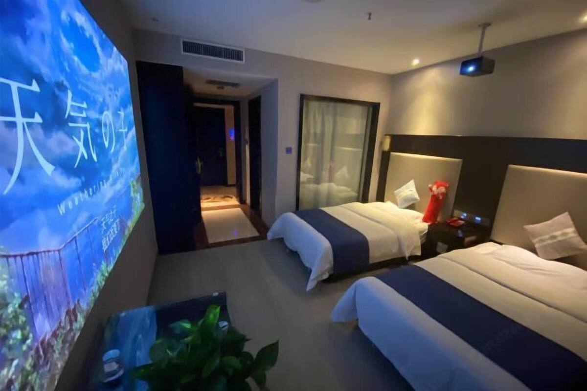 A hotel room with two beds, a TV screen, and a plant.