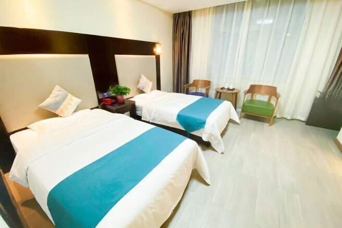 A hotel room with two beds, a nightstand, a chair, a small table, and a window with curtains.