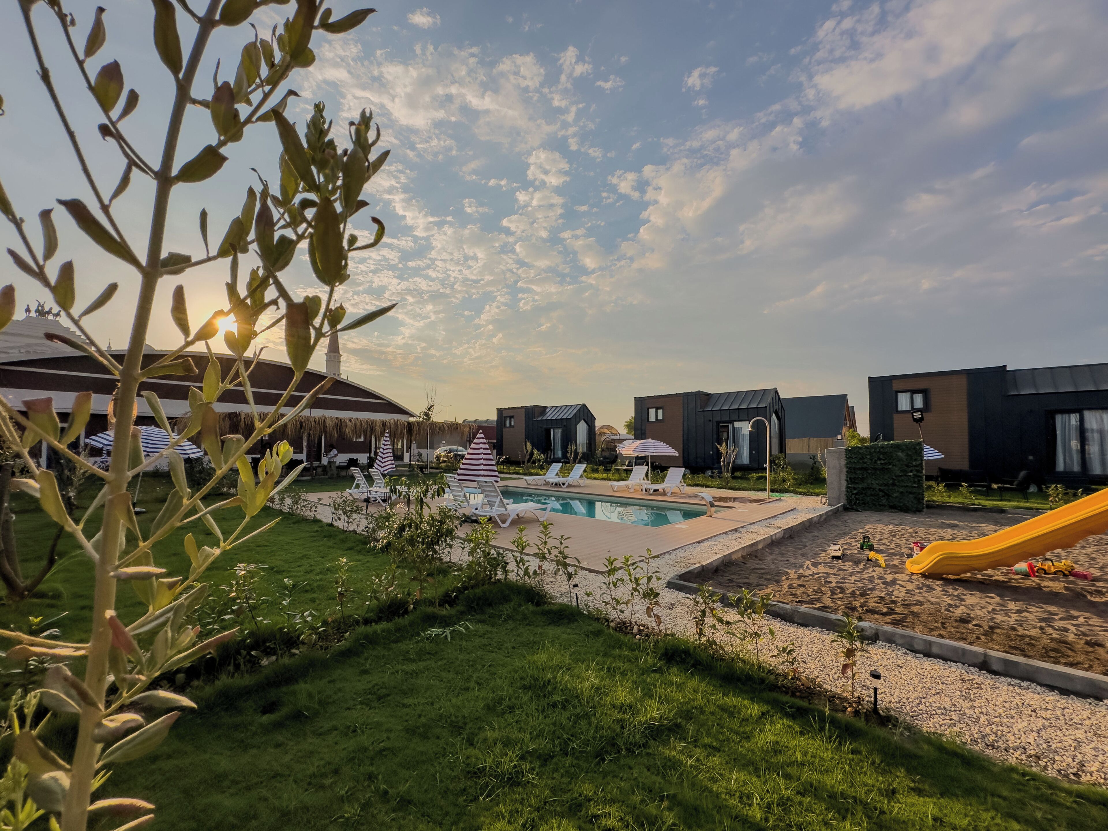 A pool area with lounge chairs and umbrellas, surrounded by greenery and modern buildings.