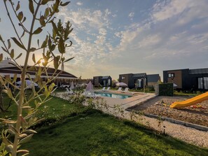 Area piscina con lettini e ombrelloni, immersa nel verde e circondata da edifici moderni.