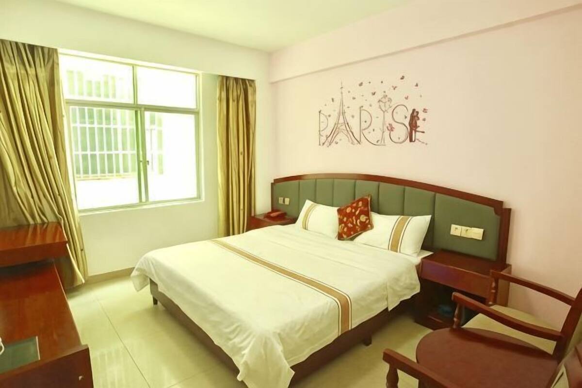 Une chambre d’hôtel comprenant un lit, un bureau, une chaise, une fenêtre avec des rideaux et un élément décoratif mural.