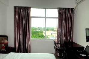 Habitación de hotel con cama, escritorio, silla, televisor y ventana con cortinas.