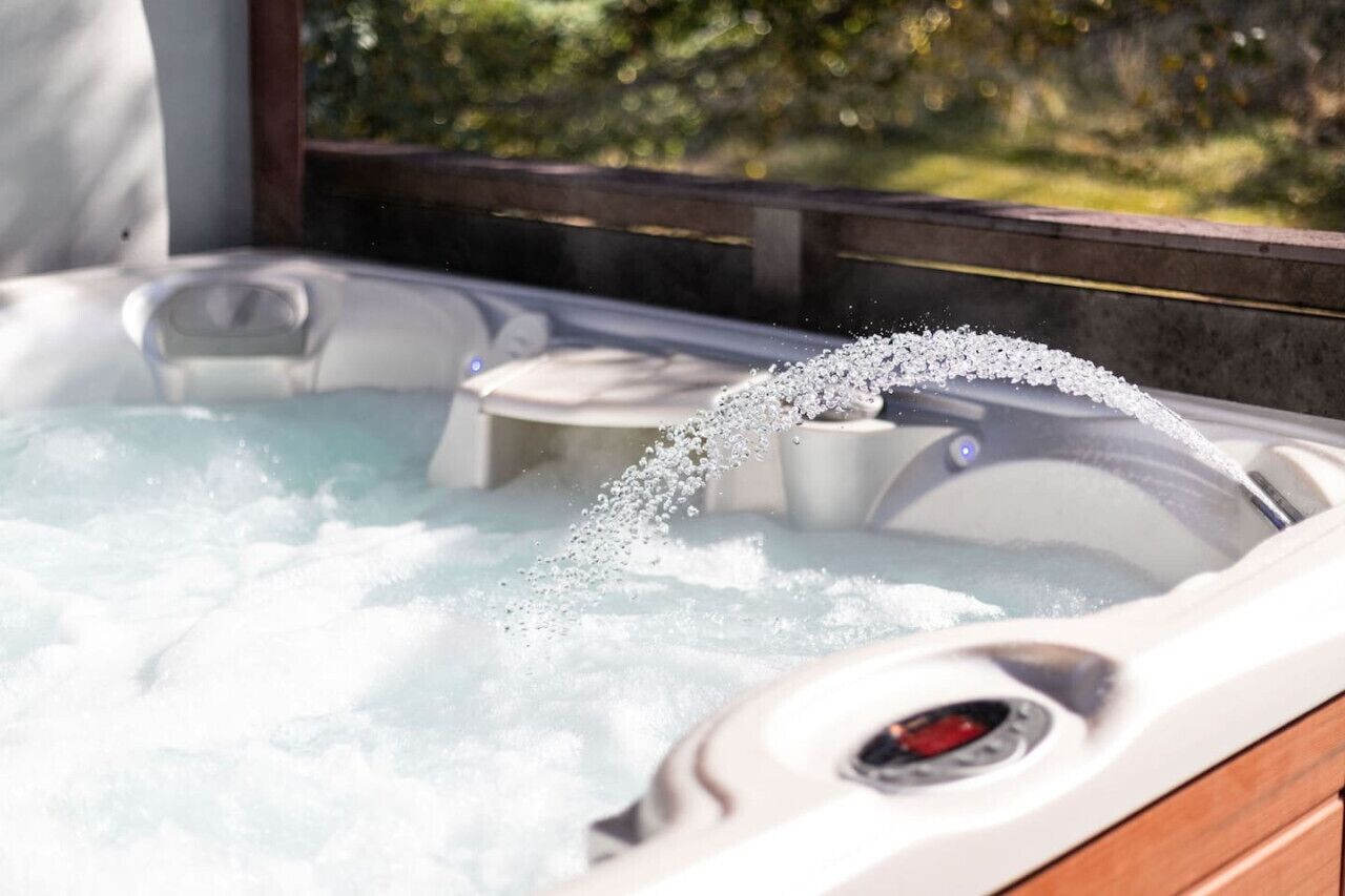 A hot tub with water and bubbles, surrounded by a wooden deck and greenery.