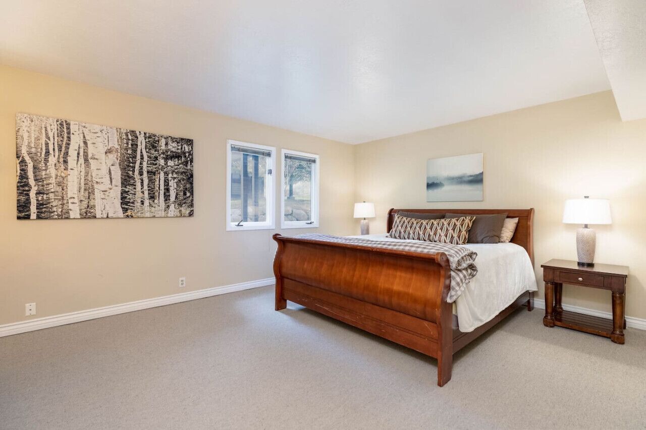 A bedroom with a large bed, two bedside tables, a window, and a wall-mounted artwork.