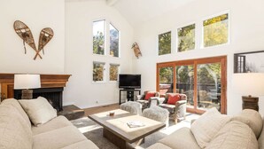A spacious living room with a fireplace, large windows, and a television.